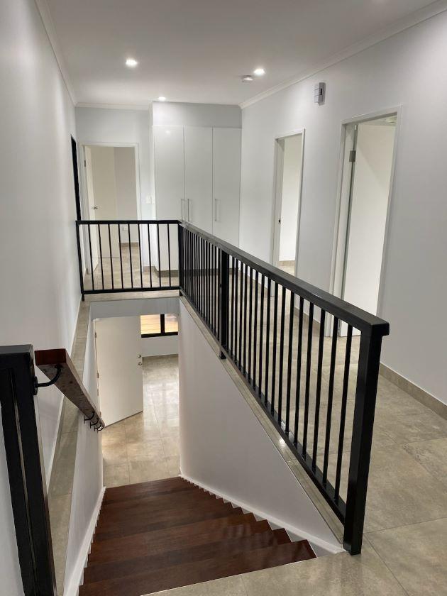 View of the landing and stairwell inside a new Katherine unit, fresh white walls, inviting lighting, pale wood flooring and sleek black bannisters.