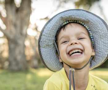 Young boy outside wearing wide brimmed hat looking up and smiling